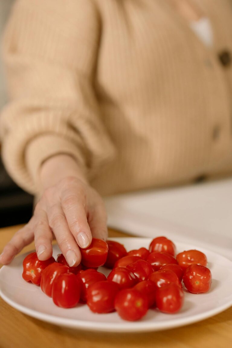 A hand reaches for cherry tomatoes on a ceramic plate, emphasizing fresh, nutritious food.